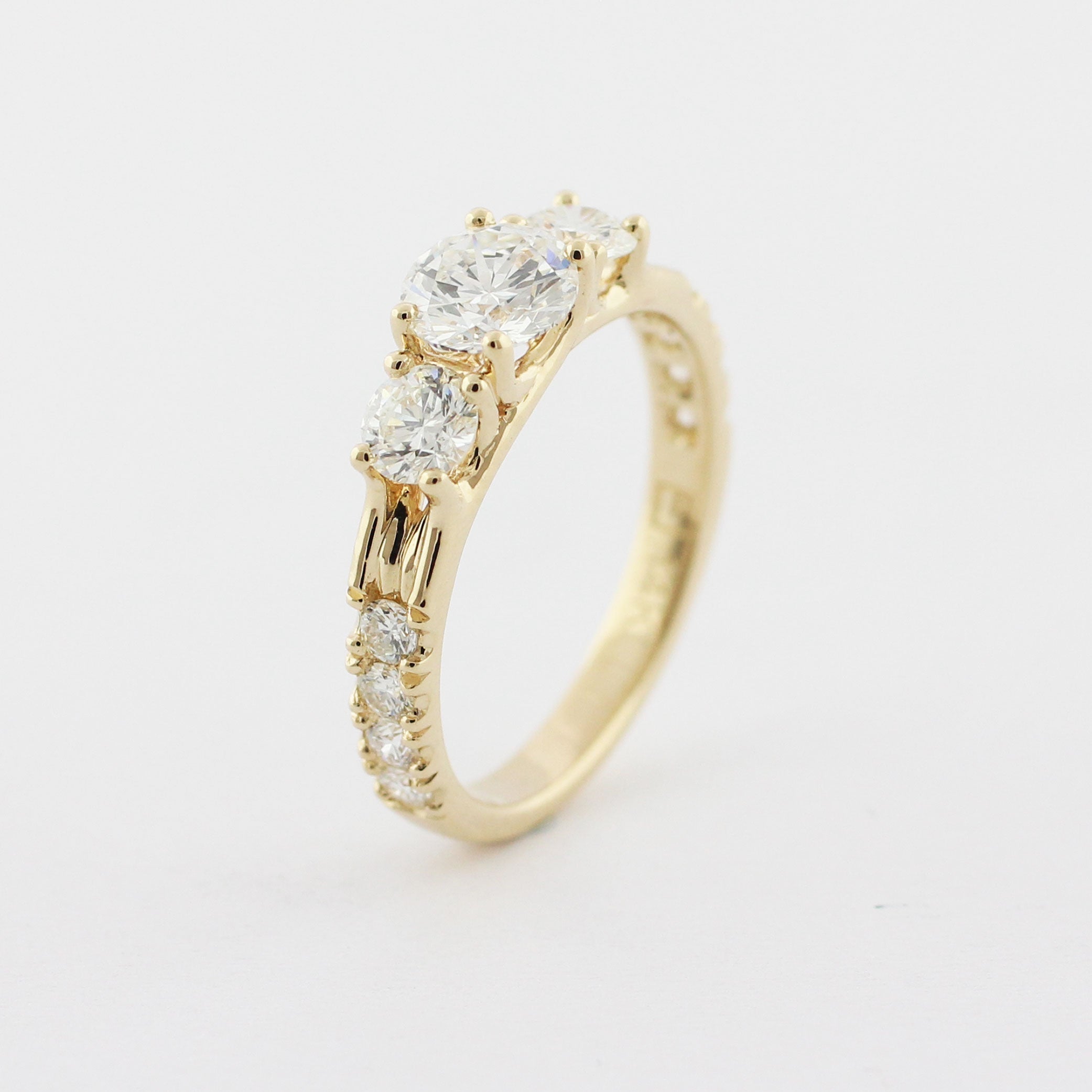 Custom 14k yellow gold three stone trellis ring with a round brilliant cut center diamond. Two prong-set accent diamonds are set on either side with a hand-cut scoop and split bead setting.