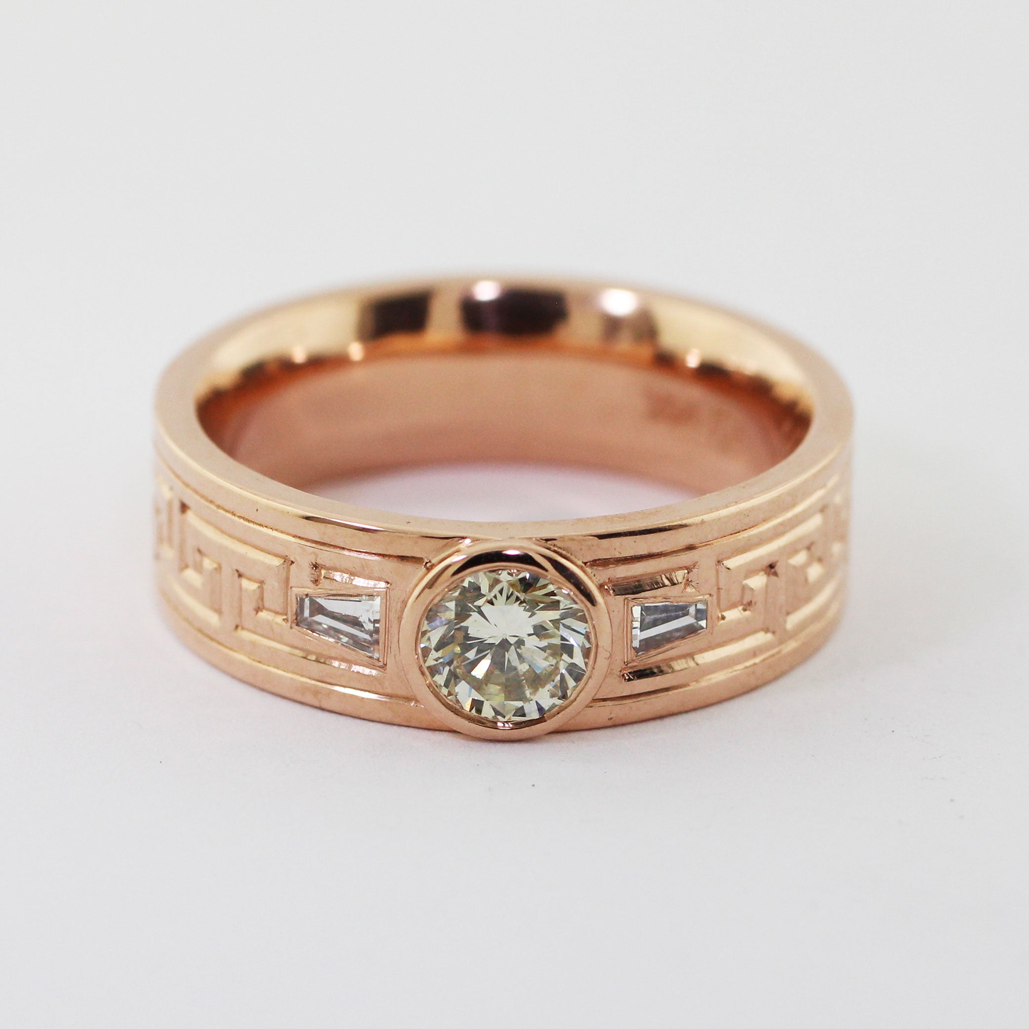 Crafted from 14kr gold and utilizing heirloom diamonds this custom men's ring features a timeless Greek key pattern expertly engraved on the exterior. Two tapered baguettes are set on either side of the center diamond.