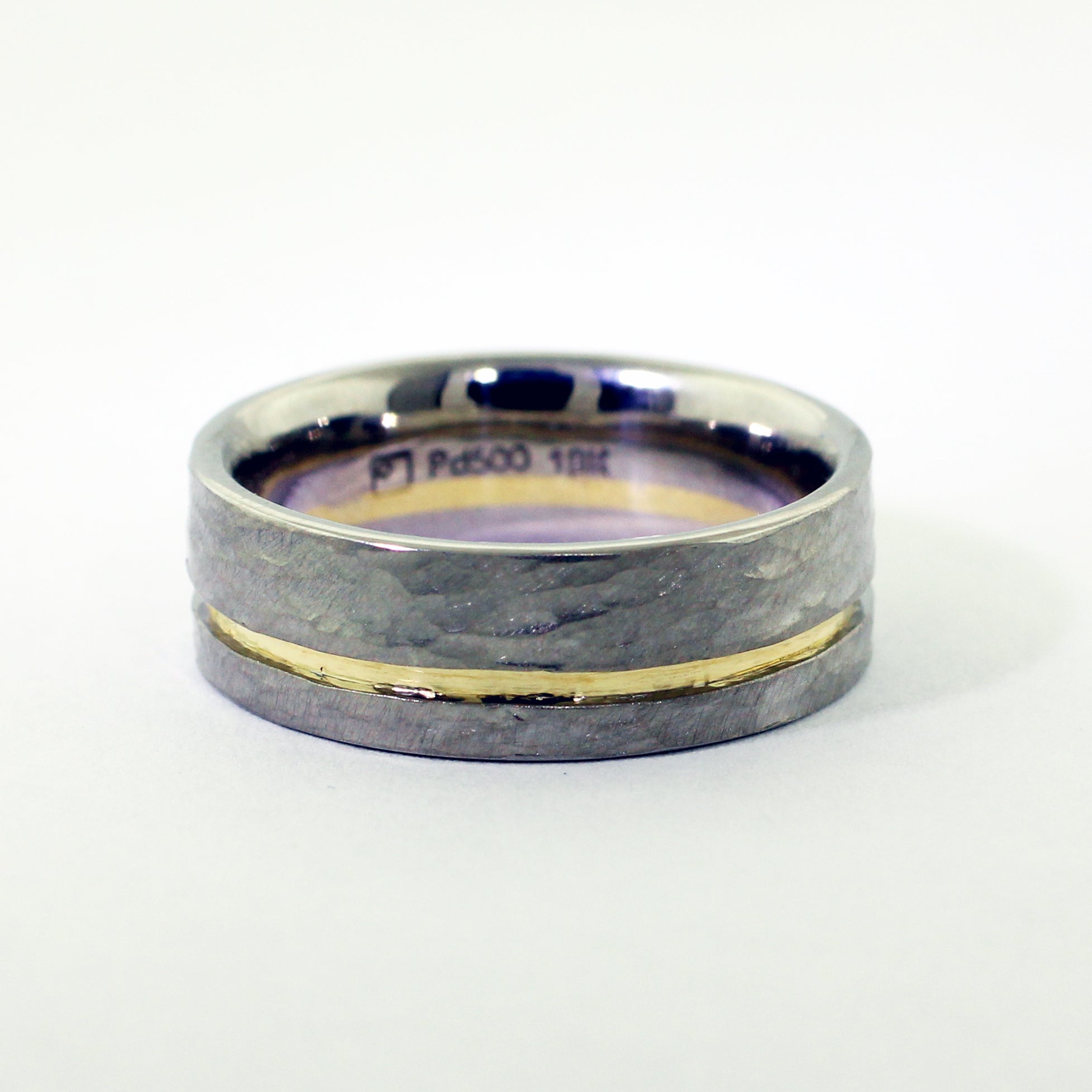 Crafted from palladium, renowned for its durability and sleek aesthetic, this men's wedding band features a warm 18ky gold recessed channel. The surface of the ring is adorned with a distinctive hammer texture, lending it a rugged yet refined appeal.