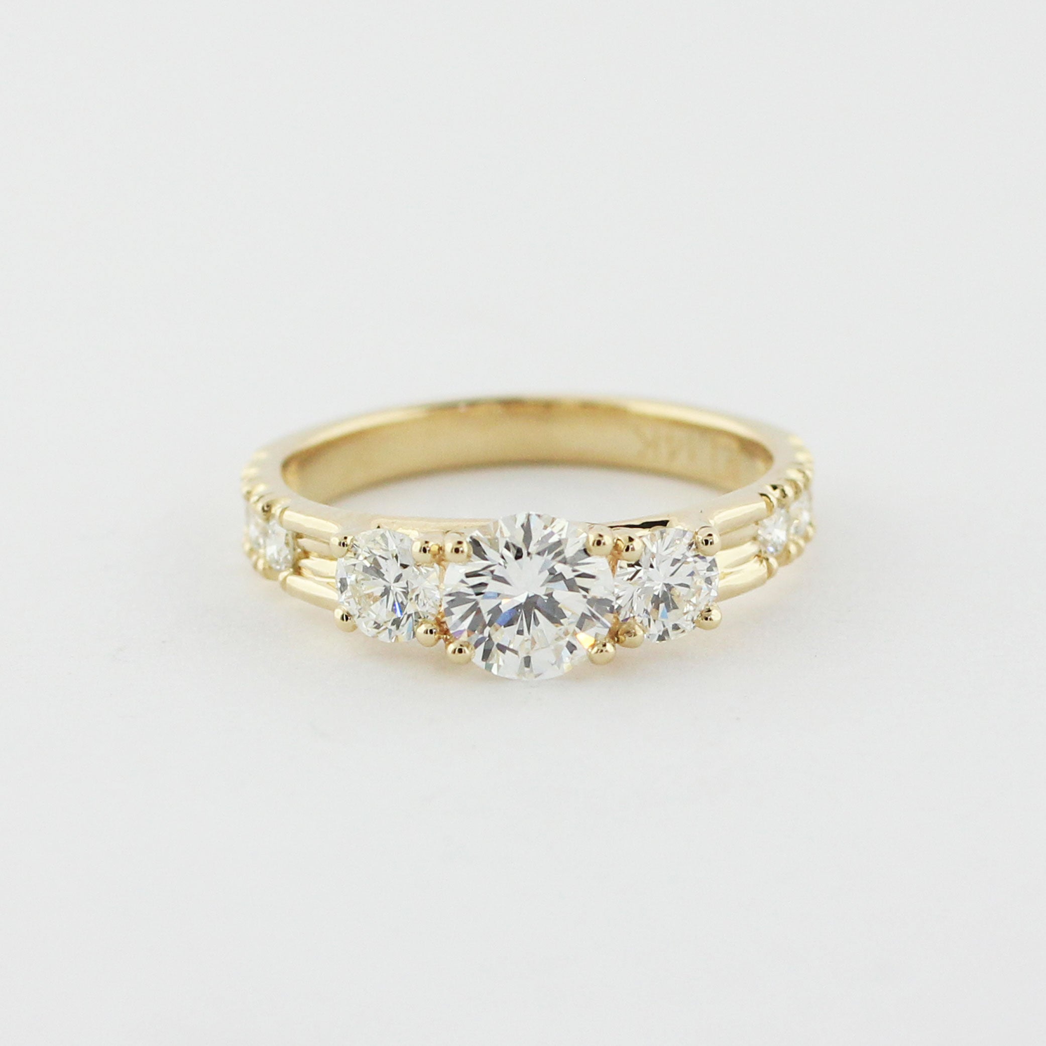 Custom 14k yellow gold three stone trellis ring with a round brilliant cut center diamond. Two prong-set accent diamonds are set on either side with a hand-cut scoop and split bead setting.