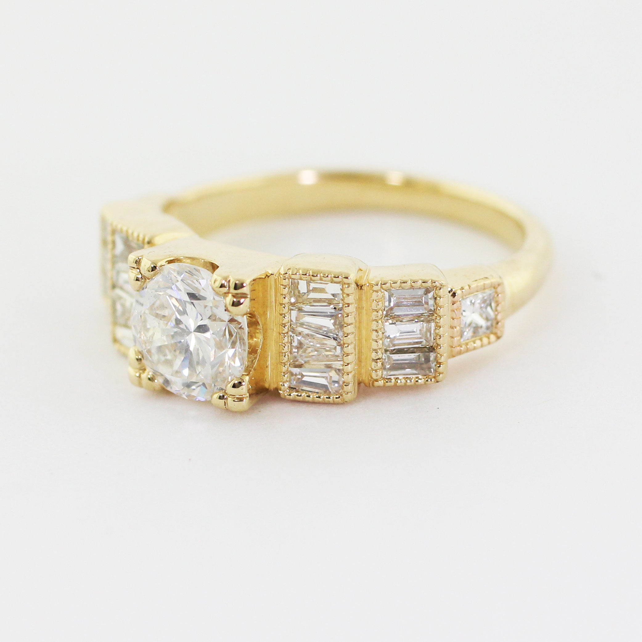 Custom 14k yellow gold Art Deco engagement ring with a prong-set center diamond and a series of heirloom diamonds channel-set along the band in a step-down pattern