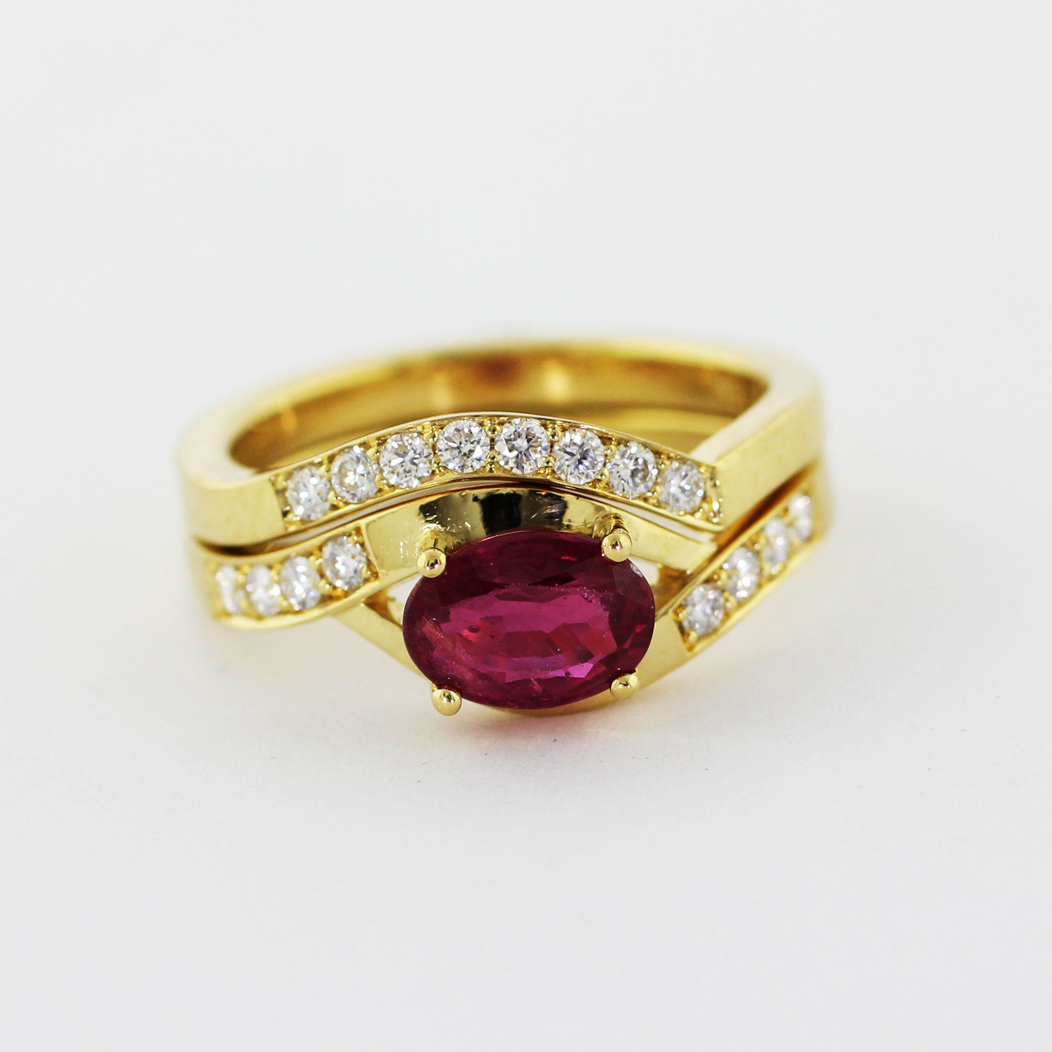 Custom 18k yellow gold engagement ring and matching wedding band, hand-fabricated with a bypass-style crown. The engagement ring features a brilliant prong-set center ruby with four 2.2mm diamonds on each side. The matching shadow band boasts the same square-edged shank adorned with eight 2.2mm bead-set diamonds.