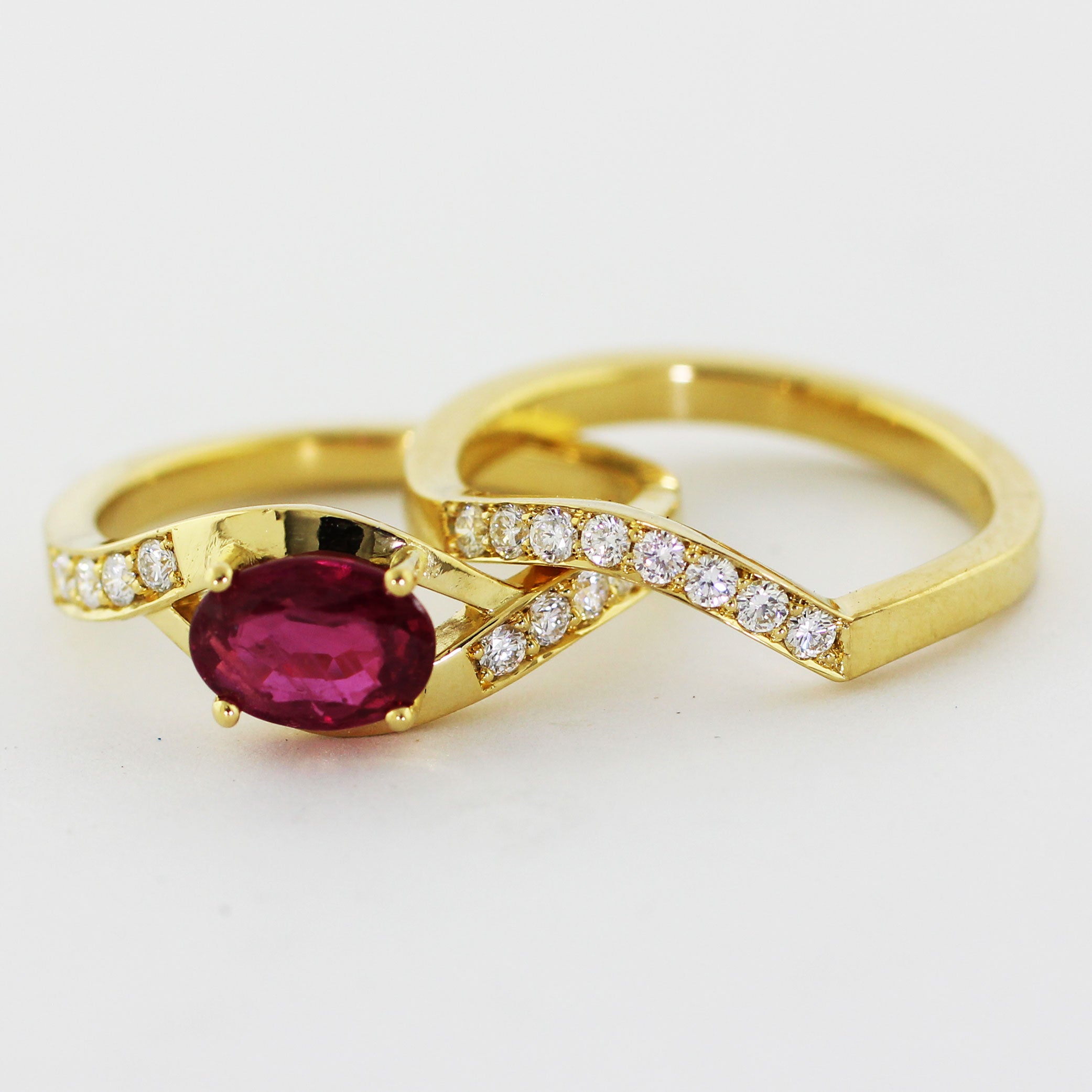 Custom 18k yellow gold engagement ring and matching wedding band, hand-fabricated with a bypass-style crown. The engagement ring features a brilliant prong-set center ruby with four 2.2mm diamonds on each side. The matching shadow band boasts the same square-edged shank adorned with eight 2.2mm bead-set diamonds.