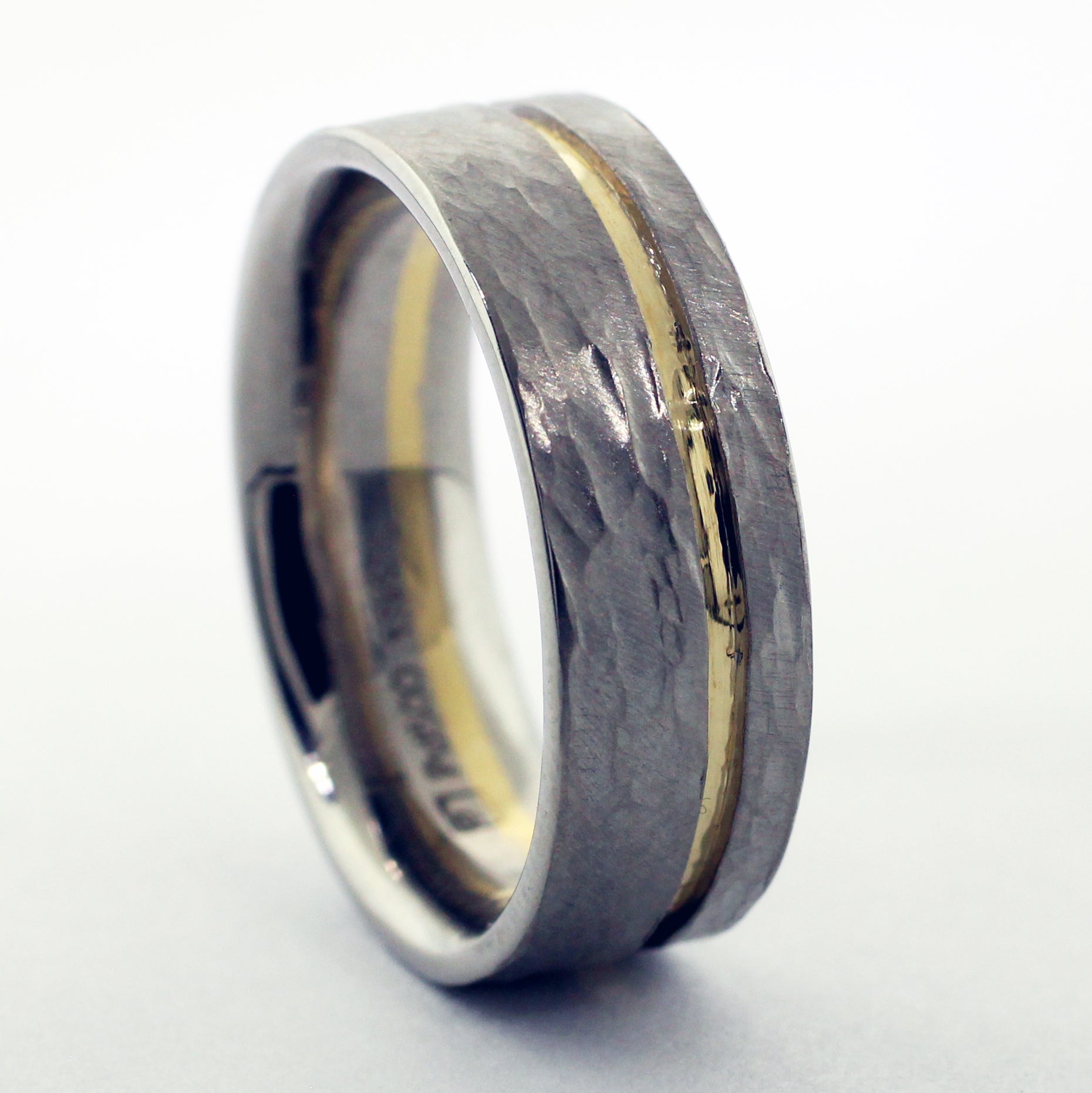 Crafted from palladium, renowned for its durability and sleek aesthetic, this men's wedding band features a warm 18ky gold recessed channel. The surface of the ring is adorned with a distinctive hammer texture, lending it a rugged yet refined appeal.