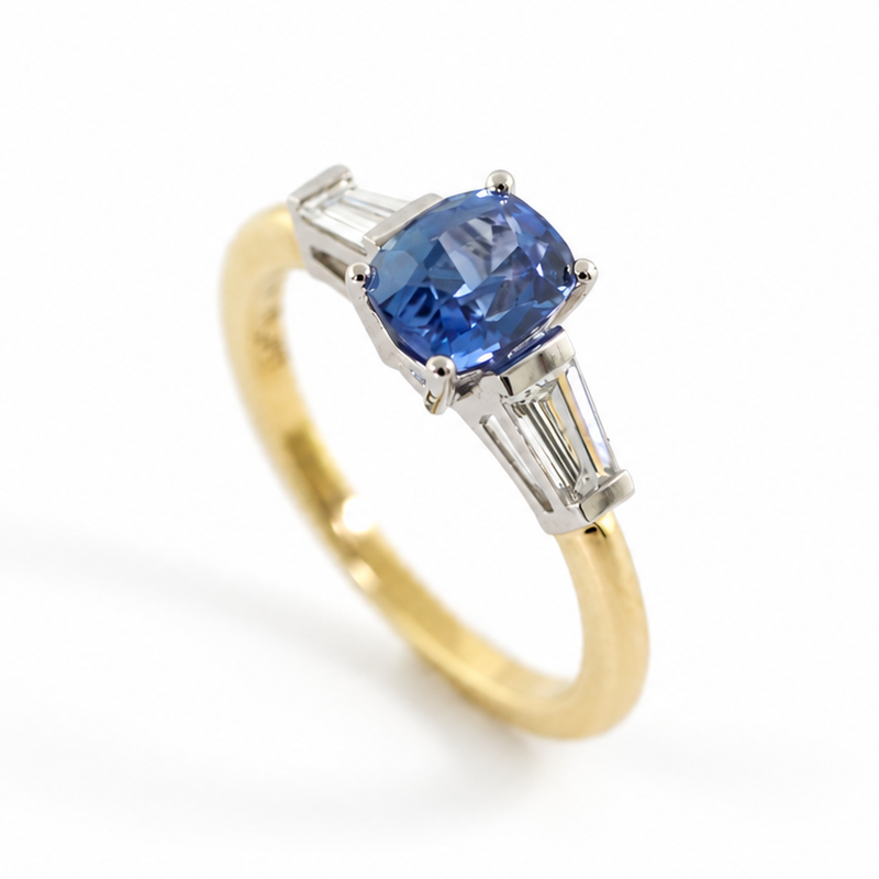 The Rainbolt ring with a cushion cut blue sapphire center stone and tapered baguette side stones in a classic basket setting.
