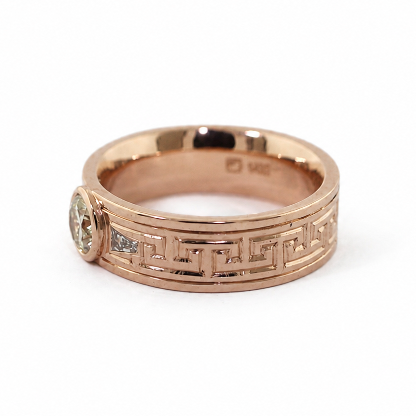 Peterman diamond ring with a round brilliant cut center stone, baguette side stones, and hand-engraved Greek key pattern.