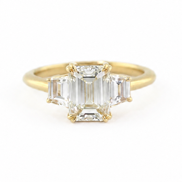 Clara engagement ring with a 1.5 ct emerald cut diamond, trapezoid side diamonds, and 14k yellow gold band.