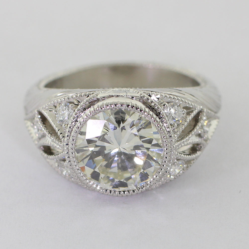Custom platinum art deco ring featuring a round brilliant center diamond, six accent diamonds, milgrain detailing, and an engraved wheat leaf pattern.